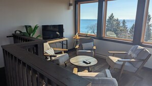 Uma sala de estar moderna com televisão, assentos e uma grande janela com vista para o mar.