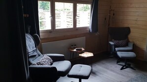 Une pièce comprenant un canapé, un fauteuil, une petite table et une fenêtre avec des stores.