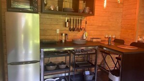 A compact kitchen with a stainless steel refrigerator, a microwave, and a stove. There are hanging utensils, a sink, and a dining area with a table and chairs. - Tiny house 'Weißenthalsmühle Eichenhäuschen' with Private Terrace (Niedenstein OT Kirchberg)