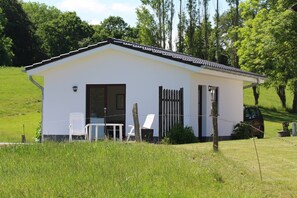 A small white building with a sloped roof, a door, and two white chairs outside.