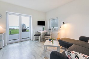 A modern living room with a sofa, a table, and a TV mounted on the wall. - Holiday Home 'Ostseeblick' with Private Terrace and Sea View (Munkbrarup)