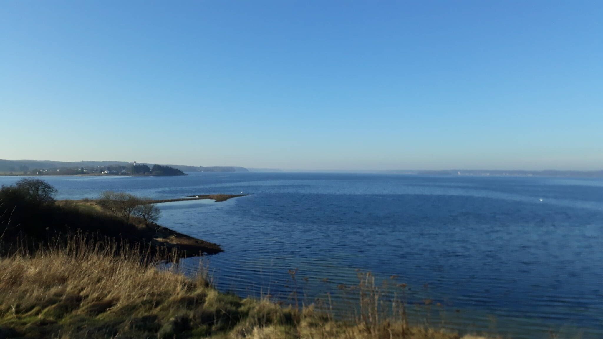 A coastal landscape with a body of water, grassy areas, and distant landforms.