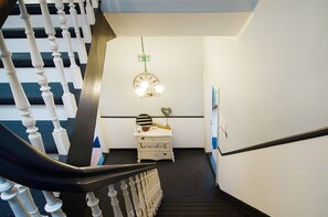 A staircase with white balusters, a white dresser with decorative items, and a wall-mounted light fixture.