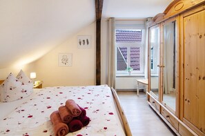 A bedroom with a bed, pillows, a bedside table, a mirror, and a window.