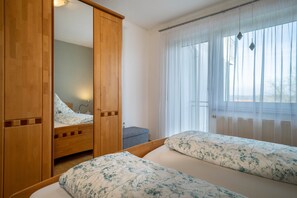 Une chambre avec deux lits, une armoire en bois, un miroir et une fenêtre avec des rideaux légers.