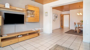 Ein modernes Wohnzimmer mit Flachbildfernseher, einer Holz-Unterhaltungsecke und einem Essbereich mit Tisch und Stühlen.