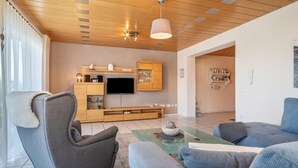 Ein modernes Wohnzimmer mit grauem Sofa, einem Couchtisch, einem an der Wand montierten Fernseher, Holzausbau und einer Decke mit Einbaustrahlern.