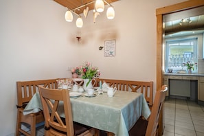 Un coin repas avec une table dressée pour quatre personnes, des chaises en bois, un vase rempli de fleurs et un luminaire fixé au mur.