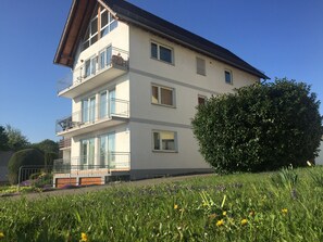 Ein mehrstöckiges Gebäude mit Balkonen, einem Vorgarten und blauem Himmel.