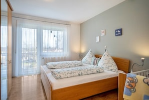 Une chambre avec un lit en bois, une fenêtre avec des rideaux légers et un mur orné d’une inscription « SOYEZ HEUREUX ».