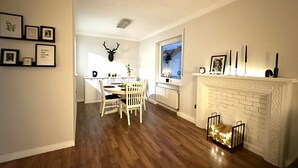 A dining area with a wooden table and chairs, a fireplace with a brick surround, and a deer head mounted on the wall.