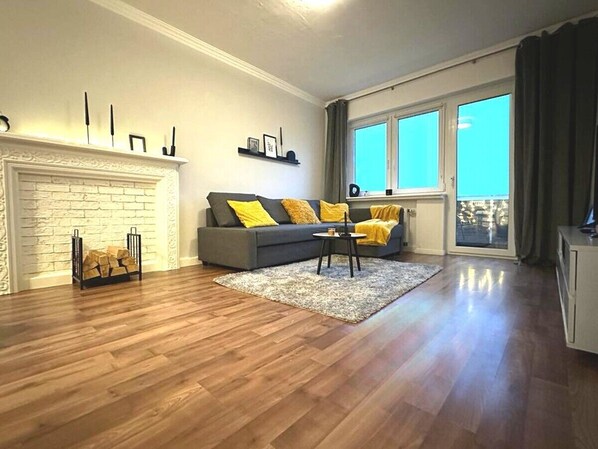 Un salon avec une cheminée, un canapé avec des coussins jaunes, une table basse et une grande fenêtre avec des rideaux.