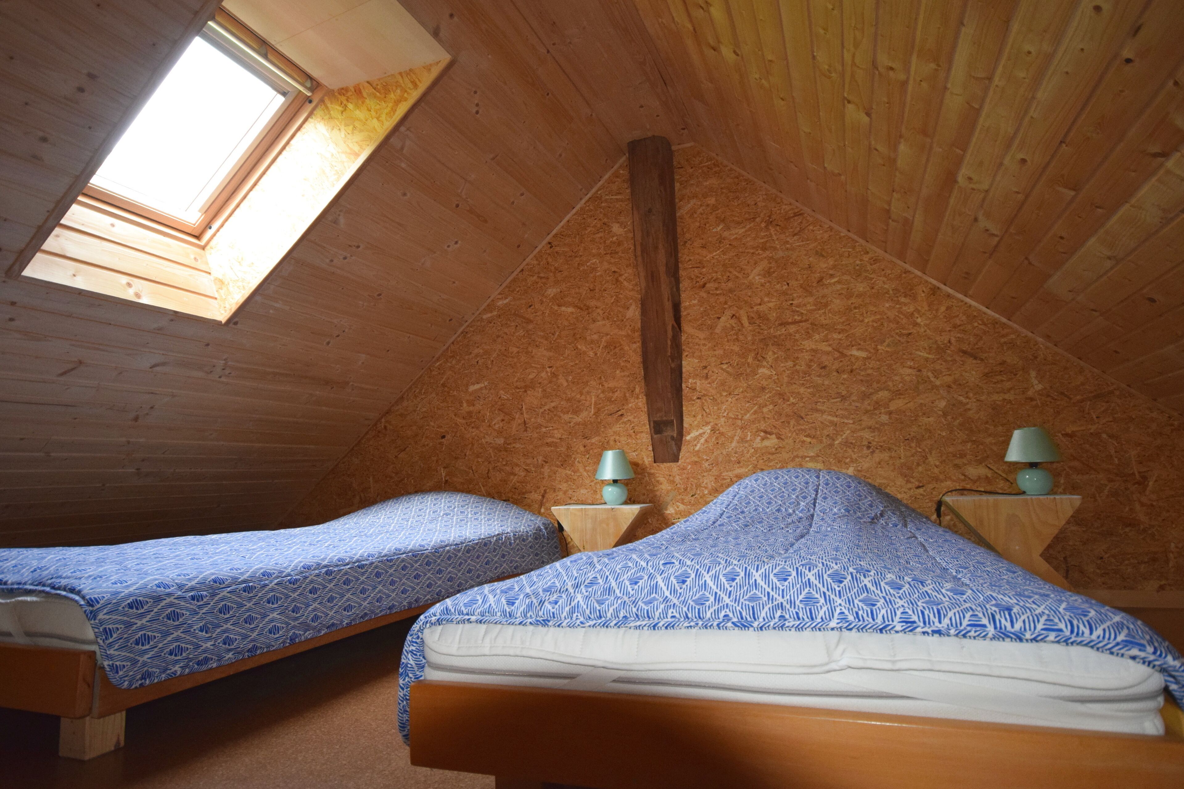 A cozy attic bedroom with two beds, wooden walls, and a skylight.