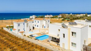 Zona residencial costera con edificios blancos, piscina y paneles solares.