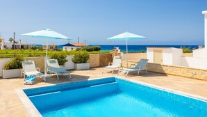 Piscina con sillones reclinables y sombrillas, con vista a la costa.
