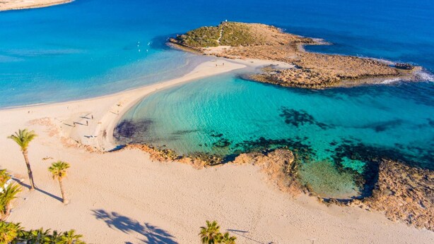 Una playa costera con aguas turquesas cristalinas, orillas de arena y afloramientos rocosos.