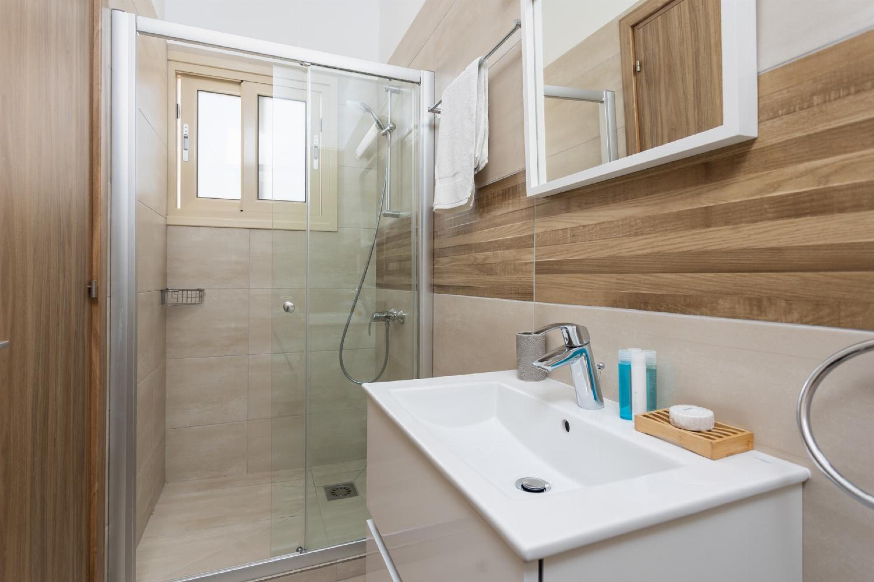 A modern bathroom with a glass-enclosed shower, a white sink, and wooden paneling on the walls.
