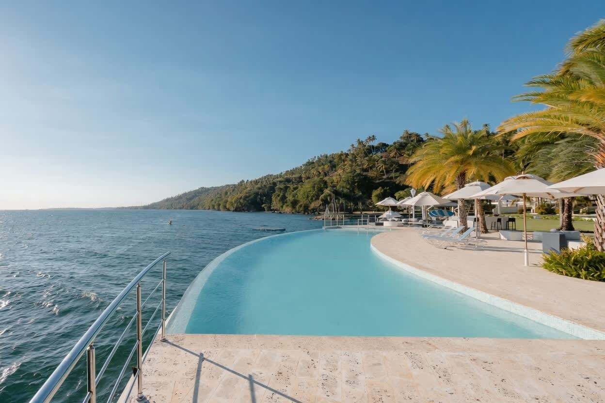 Un espace aménagé au bord de la piscine offrant une vue dégagée sur la mer, avec des chaises longues, des parasols et un accès à la plage.