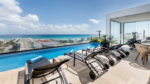 A modern rooftop pool area with a view of the ocean and cityscape. - Rooftop oceanview pool, gym, nightlife & beach (Playa del Carmen)