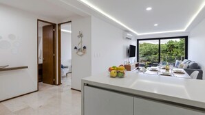 A modern kitchen with a dining area, a large window with a view of greenery, and a built-in TV. - Rooftop oceanview pool, gym, nightlife & beach (Playa del Carmen)
