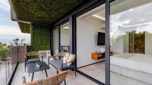 A modern balcony with wicker furniture, a glass door leading to a living area, and a green wall. - Rooftop oceanview pool, gym, nightlife & beach (Playa del Carmen)