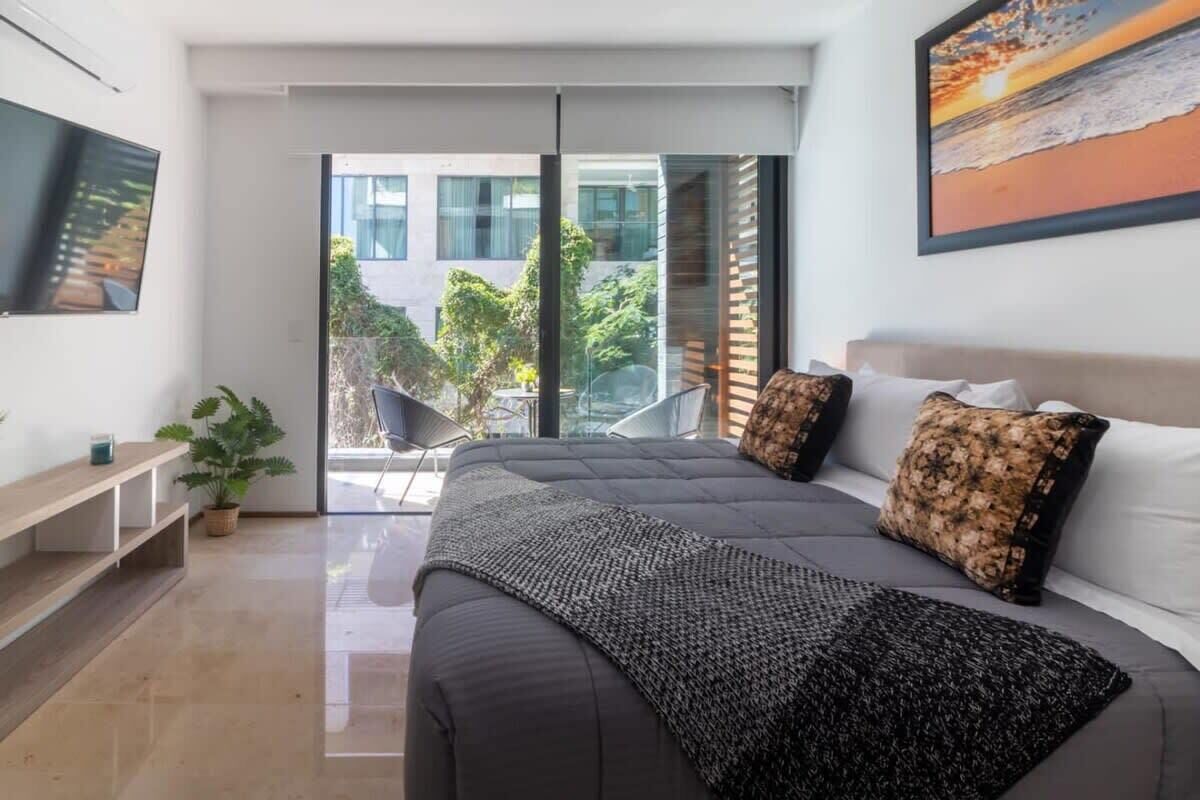 Een moderne slaapkamer met een groot bed, een flatscreen televisie en een balkon met uitzicht op gebouwen en groen.