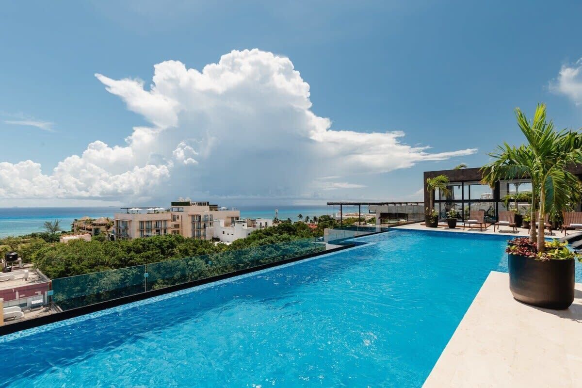 A rooftop infinity pool with a view of the ocean and surrounding buildings.