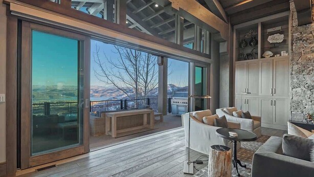 A spacious living area with a large sliding glass door leading to a balcony, a sofa, a coffee table, and a stone wall with decorative items. - Dreamscape 365 | Ski-In/Ski-Out, Arcade & Hot Tub (Park City)