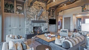 Un salon moderne avec une cheminée en pierre, des poutres en bois et un téléviseur à écran plat.