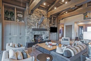 Un salon moderne avec une cheminée en pierre, des poutres en bois et un téléviseur à écran plat.