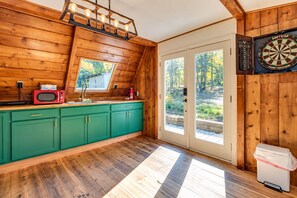 A kitchen with wooden walls, a green countertop, a microwave, and a window.