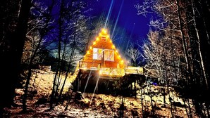 Eine Holzhütte, umgeben von Bäumen, beleuchtet von warmem Licht.