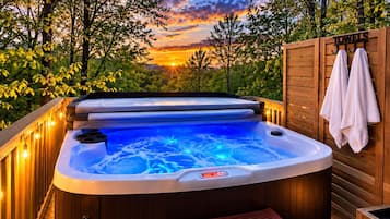 A hot tub with a wooden deck, surrounded by trees, and a sunset in the background.