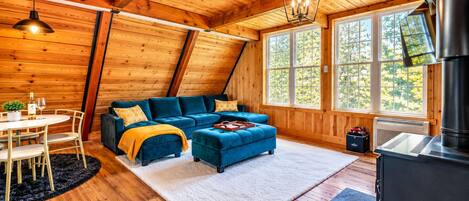 L’intérieur d’un chalet accueillant, avec un plafond en bois, un canapé bleu, une table à manger avec des chaises et une cheminée.