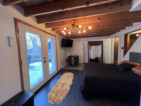 A bedroom with a large bed, a wooden ceiling, a TV, and a view of the outside.