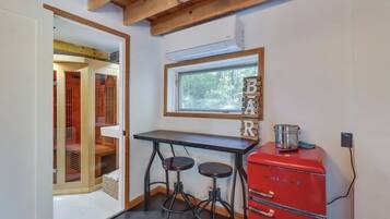 Una cocina compacta con un refrigerador rojo Galanz, una mesa de madera y dos taburetes.
