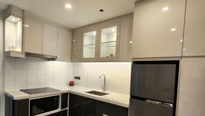 Una cocina moderna con microondas integrado, un refrigerador de acero inoxidable y un lavamanos con repisa de vidrio arriba.