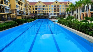 Una piscina rodeada de edificios hoteleros de varios pisos con balcones y un cielo azul despejado.