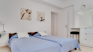 Une chambre avec deux lits, une armoire blanche, un miroir et deux tableaux accrochés au mur.