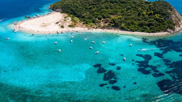 Vue aérienne d’une île tropicale avec une plage, des eaux turquoise et limpides, et des bateaux.