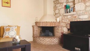 A living room with a brick fireplace, a sofa with patterned cushions, a coffee table, and a flat-screen TV. - Villa Aloni in Koridallos (Zakynthos)