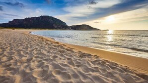 Una playa con arena y agua, una montaña lejana y un atardecer.