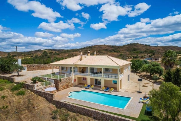 A two-story house with a swimming pool, a balcony, and a view of the surrounding hills.
