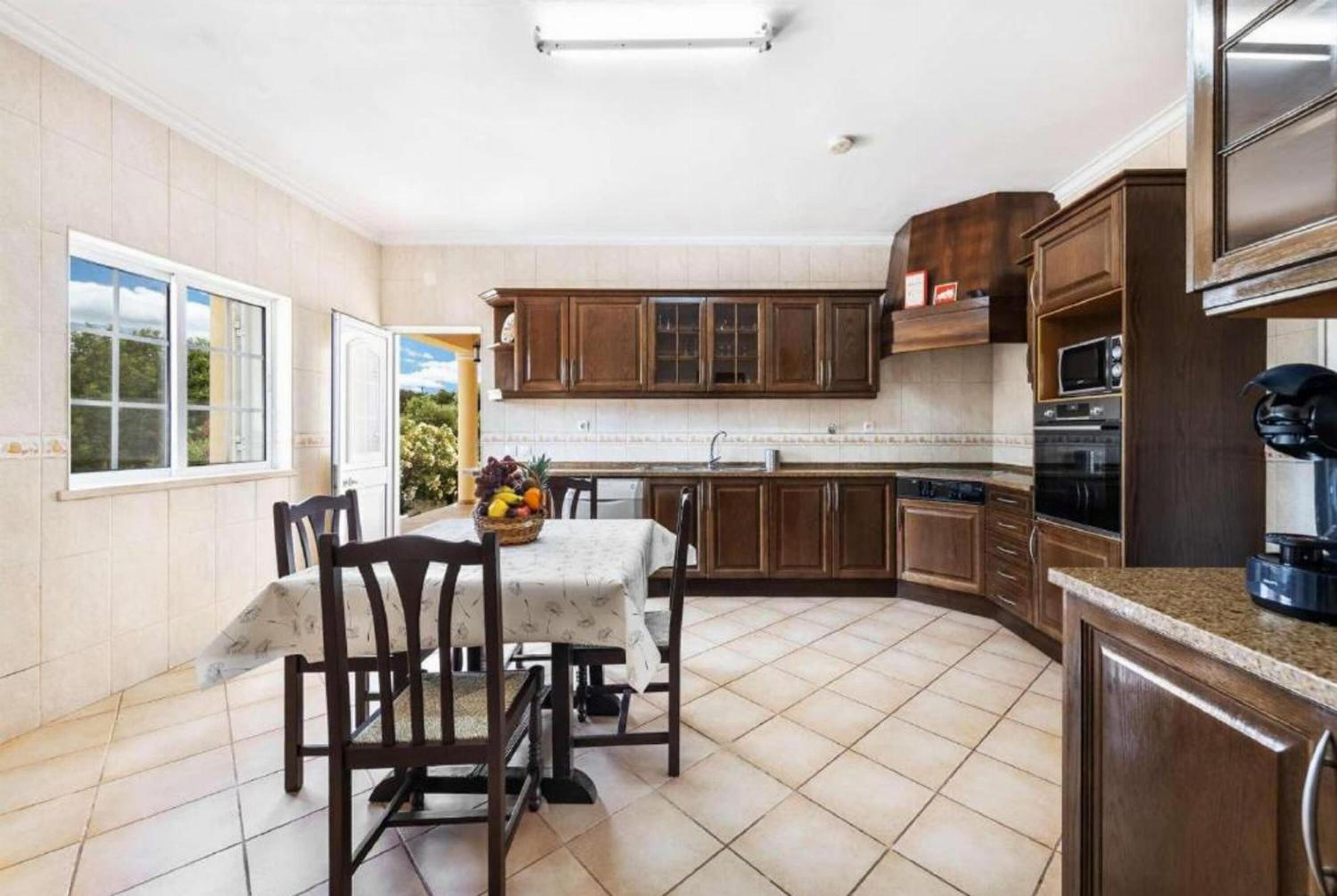 Una cocina con armarios de madera, una mesa de comedor con sillas y una ventana con vista a la vegetación.