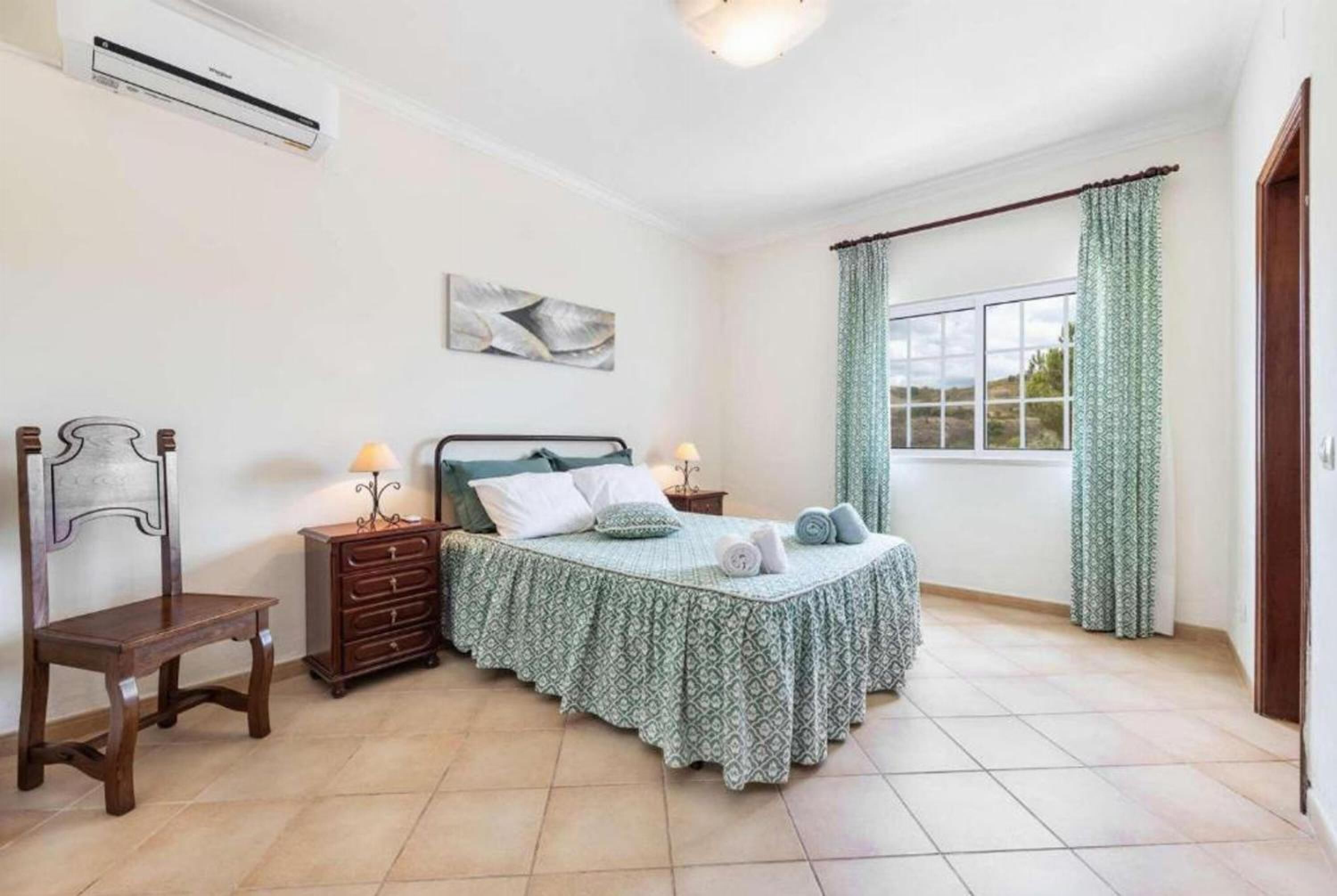 A bedroom with a bed, a chair, a dresser, and a window with curtains.