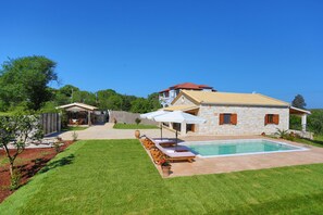 A house with a swimming pool, a patio with lounge chairs, and a garden.