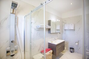 A modern bathroom with a glass shower enclosure, a sink with a mirror above, and marble walls.