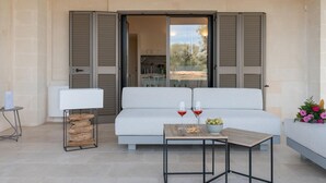 A modern outdoor seating area with a white sofa, a small table with drinks and snacks, and a lamp. - Villa Belkis 6 Emma Villas (Ostuni)