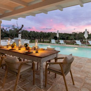 Ein Holzespeisesaal mit Stühlen, ein Pool und Lounge-Stühle im Hintergrund.