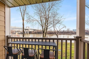 A covered outdoor area with a table and chairs, overlooking a river and a bridge.